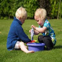 dos niños jugando con baldes o botes de agua en el pasto